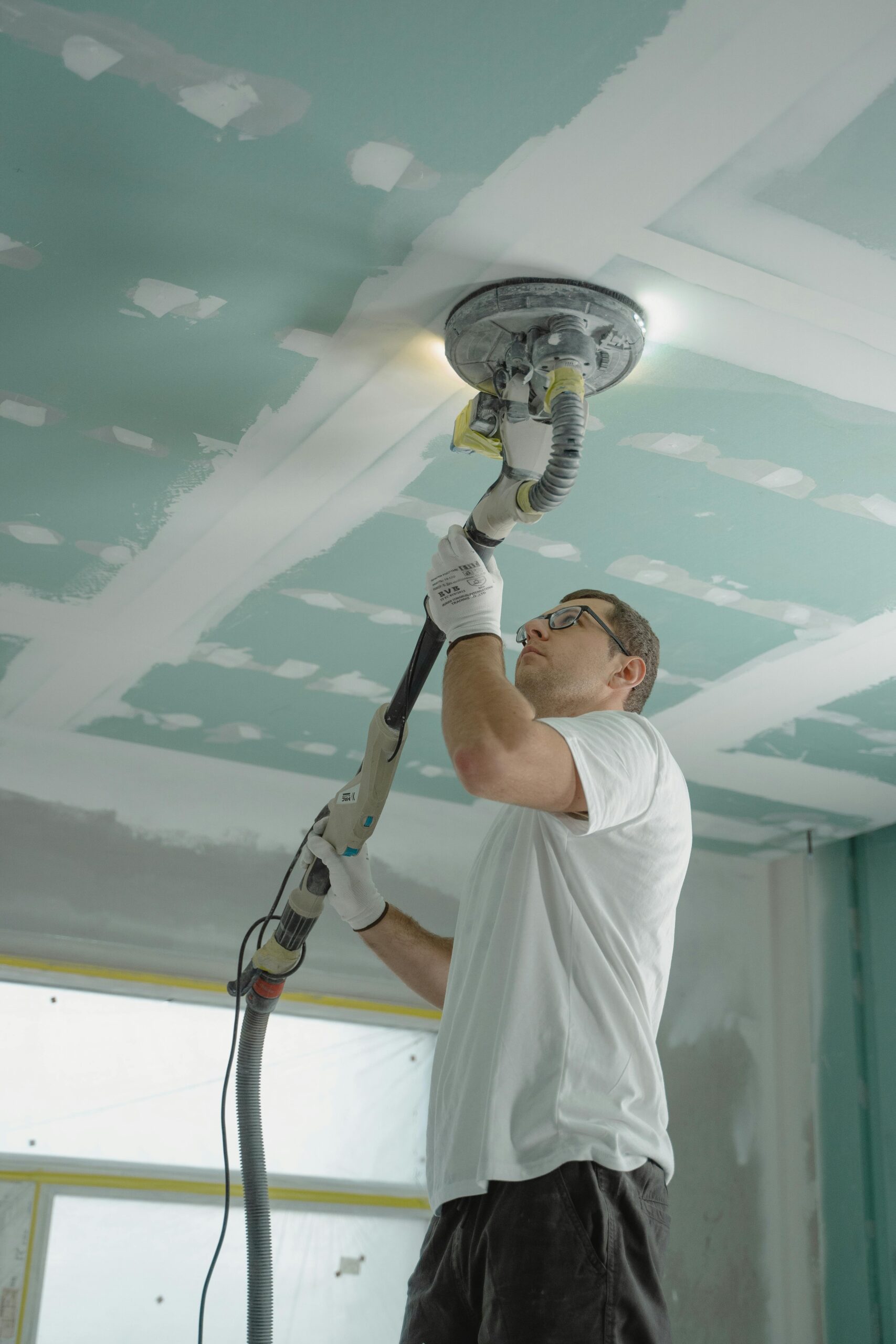 Adult male sanding a drywall ceiling with an industrial tool during home renovation.